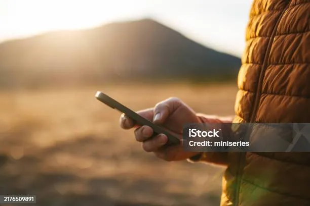 A hand holding a smartphone outdoors at sunset