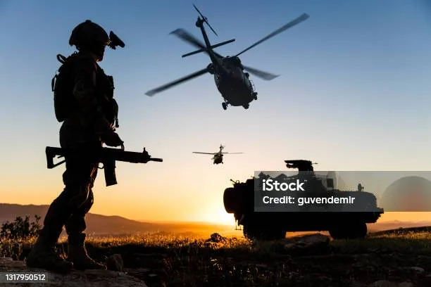 Soldier silhouetted against a helicopter at sunset